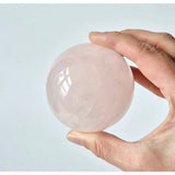 Rose quartz sphere, pink polished crystal, 63mm (350g), held in hand