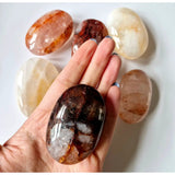 Kristal vuurkwarts palmsteen in hand with dark smoky hues; assorted polished crystals nearby