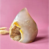 Large teardrop gray agate druzy crystal with a brown-gold cavity on pink background.