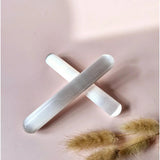 Two 15 cm selenite massage sticks, white translucent crystals crossed on a pale background