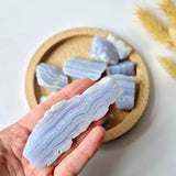Blue lace agate druzy stones, polished chunks with pale banding; several pieces held in hand over a wooden tray.