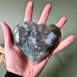 Druzy moss agate heart on metal stand, gray-green mossy patterns, held in hand
