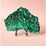 Chrysocolla/Malachiet edelsteen slab op zwarte metalen standaard, groene banding tegen roze achtergrond