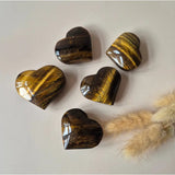 Five heart-shaped tiger's eye palmstones with golden-brown banding, polished.