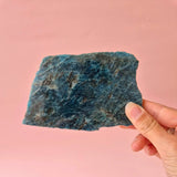 XXL blue apatite slab held in hand against pink backdrop.