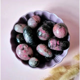 Rhodonite palm stones (3–5 cm) polished trommelstones in pink-black patterns in a purple bowl