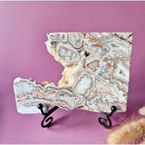 Crazy Lace Agate slab with banded pink, white and brown patterns on a black display stand, 208 g