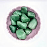 Kristalgroen kwarts getrommeld; groene edelstenen in een roze schaaltje, meerdere stuks 3–8 cm