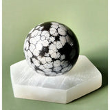 Snowflake Obsidiaan bol, 4–5 cm, zwart met witte vlokken op witte hexagonale sokkel