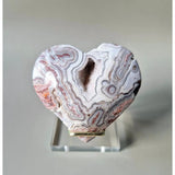 Mexican Crazy Lace Agate heart on clear display stand with pink, white and gray banding and a hollow cavity.