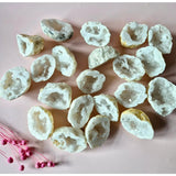 Witte agaat geoden (5–7 cm), druzy edelsteen met glans; meerdere geoden verspreid op roze achtergrond