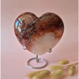 XXL fire quartz heart crystal with hematite inclusions on a metal display stand, pink backdrop