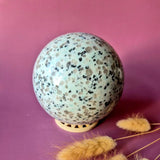 Kiwi Jasper ball by Moonlight Gemstones, 100 mm diameter, speckled green with black spots on wooden stand