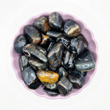 Falcon's Eye tumbled stones from Moonlight Gemstones in a purple bowl; blue-gray with golden-brown banding.