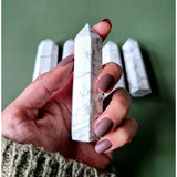 Howlite obelisk tower, white with gray veining, 8-10 cm, held in hand with extra towers in background.