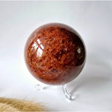 Strawberry quartz crystal sphere, 60mm, polished red-brown orb on a clear stand