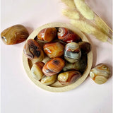 Sardonyx handstones (palm stones), polished with orange-cream banding in a wooden bowl; 11 pieces, 4–7 cm each