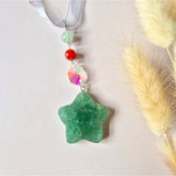 Kerstster suncatcher met edelstenen: mintgroene stervormige hanger aan lint, met zilverkleurige verbindingsringen, groene en rode kralen en iriserende facetkraal voor lichtspel in zonlicht