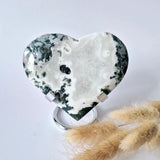 Hartvormige mosagaat druzy edelsteen op metalen standaard; wit met groene en zwarte spikkels.