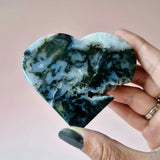 Heart-shaped moss agate druzy gemstone held in hand, blue-green pattern