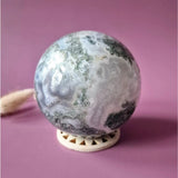Moss agate druzy geode sphere, 90mm diameter, pale gray with green moss inclusions on a display stand