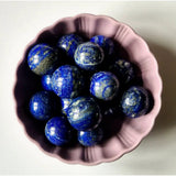 Lapis lazuli edelsteen bol, 4–5 cm, in een roze schaal vol glanzende blauwe stenen
