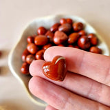 Mini edelsteen hartje zaksteen van rode jaspis, 1,5 cm, in hand met kom vol rode jasper stenen — Moonlight Gemstones