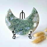 Moss agate crescent moon slab on black metal display stand with green dendritic patterns.