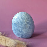 Celestite freeform gemstone in soft blue tones, with crystalline facets on a pink backdrop