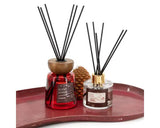 Scent Junkie Noël reed diffusers, Festive Cinnamon; two bottles in red and clear glass with black/gold caps; Home Bound